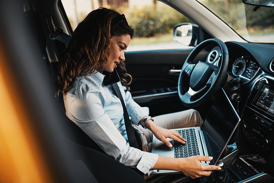 Target Zero Distracted Driving Initiative - View of a Woman Sitting in Her Car While Using a Laptop and Her Cellphone