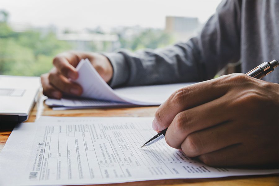 Tax Season FAQs - Closeup View of a Man Sitting at a Desk Filling Out Tax Paper Documents