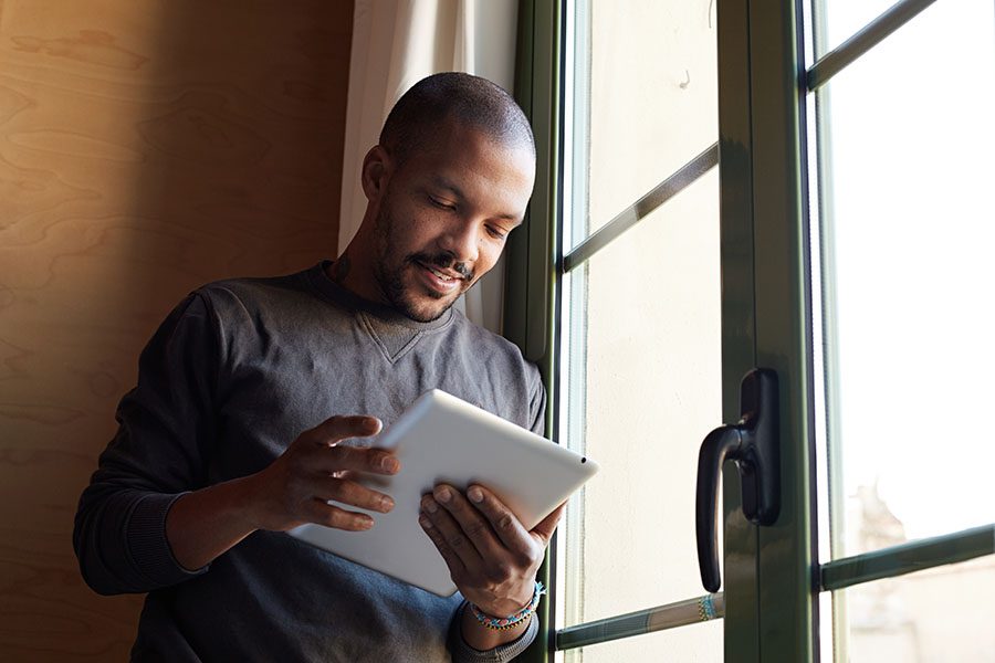 Video Library - Portrait of a Man Standing Next to a Glass Door at Home Using a Tablet