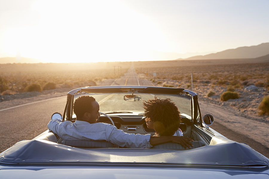 Auto Insurance Renewal - Rear View of a Couple Driving in a Convertible Towards the Sunset