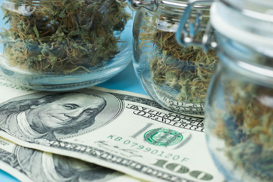 Cannabis Business Insurance Renewal - Closeup View of Jars with Dried Cannabis Sitting on Top of Hundred Dollar Bills