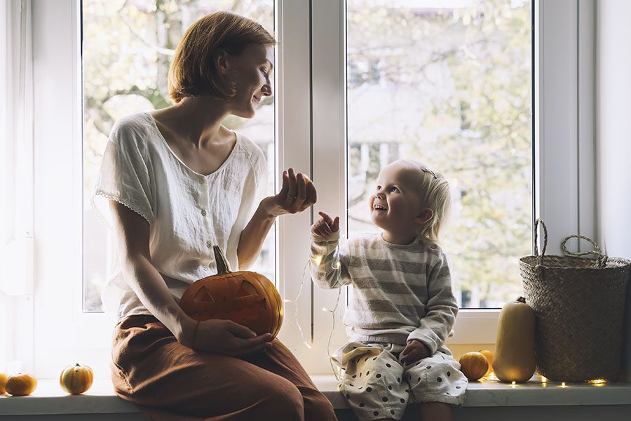 Home Insurance Renewal - View of Happy Mother and Daughter Sitting Next to the Window in Their Home Getting Ready to Carve a Pumpkin for Halloween