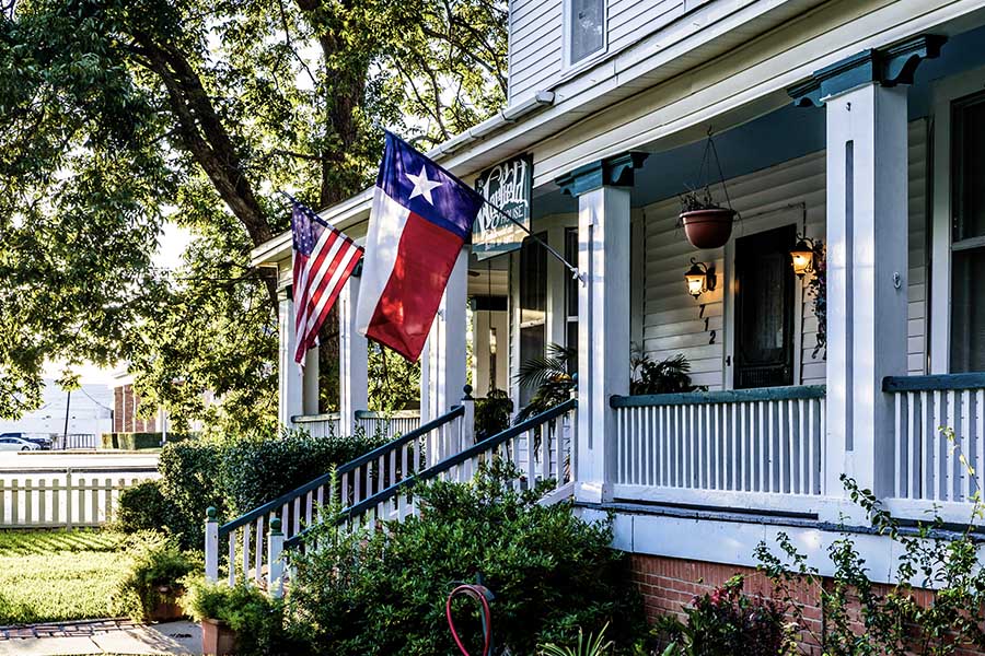 Washington Cannabis Insurance - White Modern Farmhouse with an American Flag and Texas Flag Hanging Up Off the Front Porch