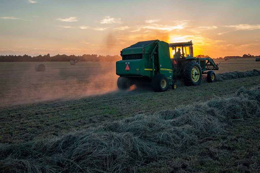 Farm Equipment Insurance - Tractor Going Down the Field and Collecting Hay Piles at Sunrise