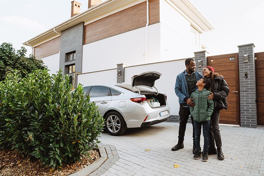 Auto Insurance & Home Insurance Renewal - Family Smiling and Starring at Each Other Outside Their Home in Front of Their Car with the Trunk Open on a Cold Nice Day