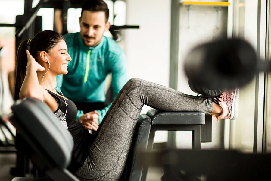 Personal Trainer Insurance - Smiling Woman Exercising in the Gym With the Help of Her Personal Trainer While Listening to Music